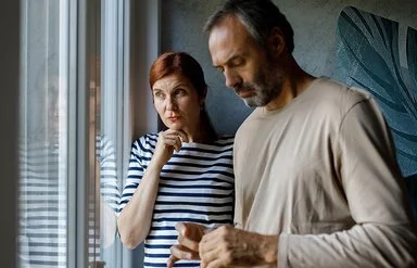 Eine Frau und ein Mann stehen nachdenklich vor einem Fenster.