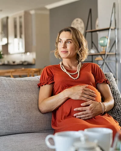 Eine Frau mit Risikoschwangerschaft sitzt auf dem Sofa und hält ihren Bauch.