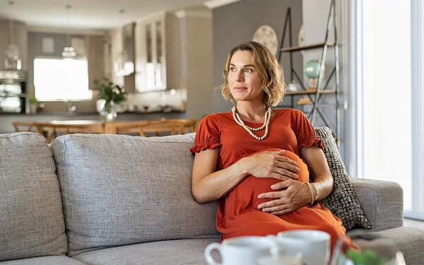 Eine Frau mit Risikoschwangerschaft sitzt auf dem Sofa und hält ihren Bauch.