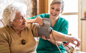 Junge Frau vom ambulanten Pflegedienst misst den Blutdruck einer zu pflegenden älteren Seniorin.