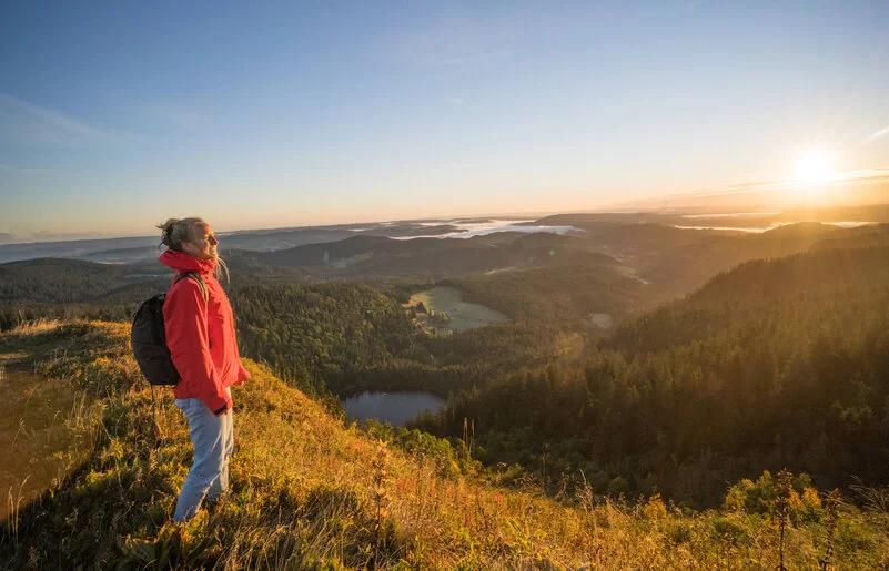 Eine Frau steht auf einem Berg. Vor ihr erstreckt sich der Schwarzwald im Sonnenaufgang.