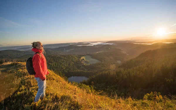 Eine Frau steht auf einem Berg. Vor ihr erstreckt sich der Schwarzwald im Sonnenaufgang. 