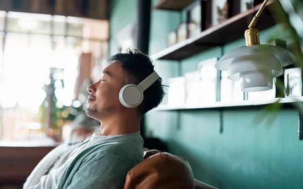 Junger Mann sitzt entspannt auf dem Sofa und hört die Podcasts der AOK NordWest.