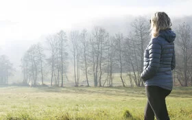 Frau geht bei einer Gehmeditation über eine Wiese.