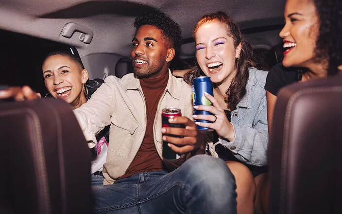 Vier junge Menschen auf der Rückbank eines Autos. Einige halten Getränkedosen in der Hand.