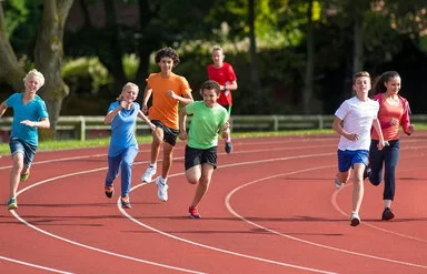 Es ist eine Gruppe Kinder zu sehen, die auf einer professionellen Laufbahn ein Rennen gegeneinander laufen.