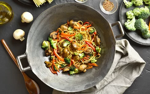 Wokpfanne mit Brokkoli, Pilzen, Paprika und Nudeln aus der Vogelperspektive.