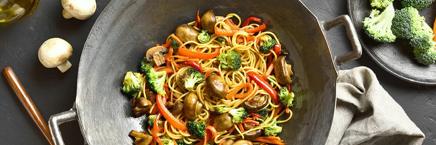 Wokpfanne mit Brokkoli, Pilzen, Paprika und Nudeln aus der Vogelperspektive.