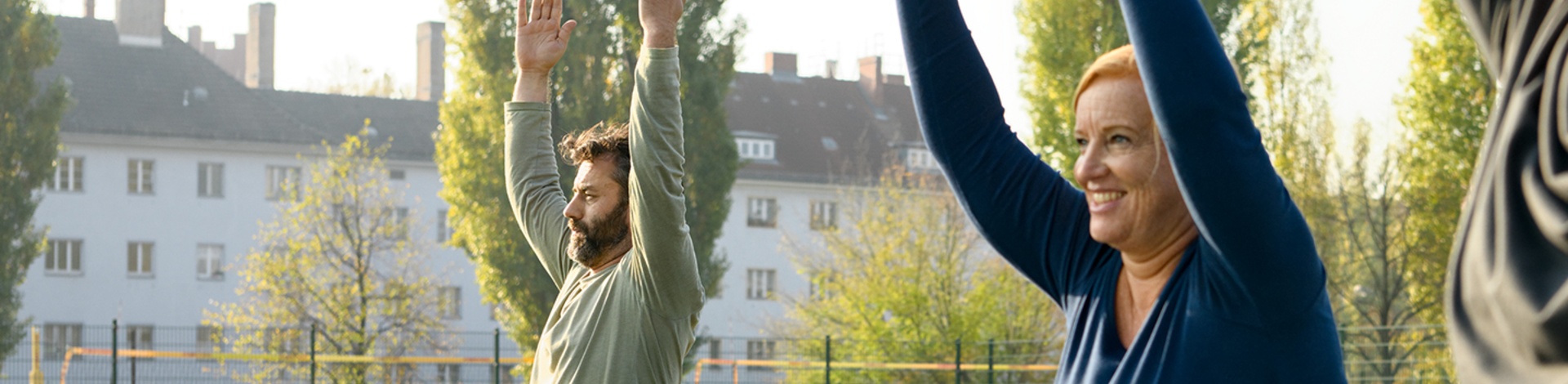 Drei Menschen stehen draußen auf einer Wiese und machen Yoga.