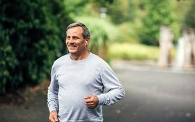 Ein Mann mittleren Alters mit grauem Langarmshirt joggt auf einem Weg in einem Park.