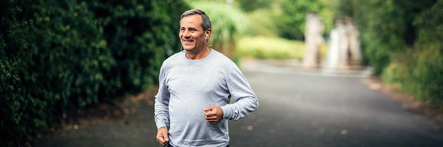 Ein Mann mittleren Alters mit grauem Langarmshirt joggt auf einem Weg in einem Park.