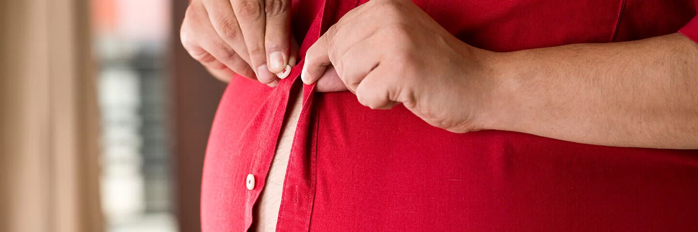 Ein Mann mit Bierbauch knöpft sich ein rotes Hemd zu.