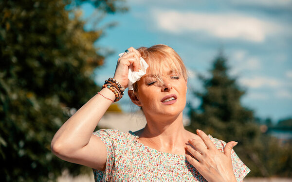 Frau in Sommerkleid tupft sich bei heißem Sommerwetter die Stirn mit einem feuchten Tuch.