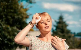 Frau in Sommerkleid tupft sich bei heißem Sommerwetter die Stirn mit einem feuchten Tuch.