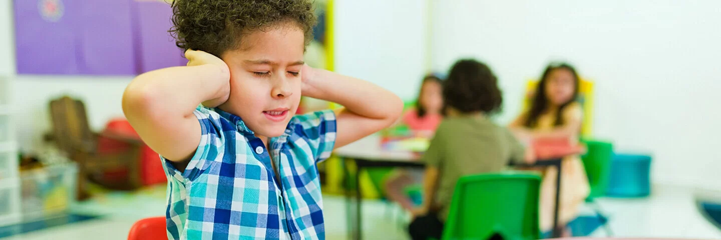 Ein hochsensibles Kind hält sich im Kindergarten die Ohren zu.