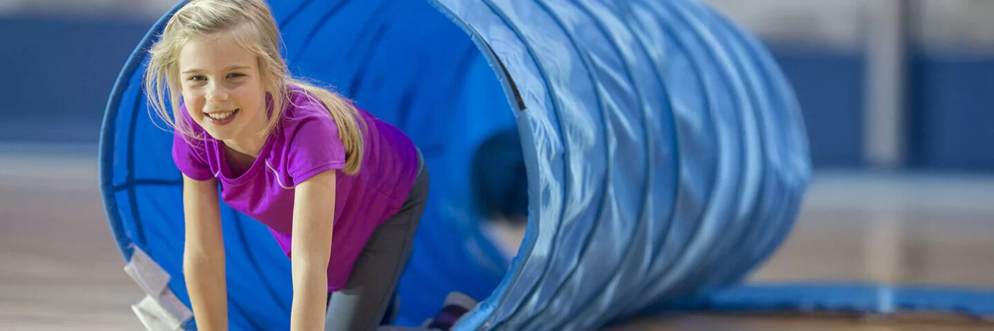 Ein blondes Mädchen im Grundschulalter spielt am AOK-Sportel-Sonntag in einem blauen Kriechtunnel.