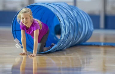 Ein blondes Mädchen im Grundschulalter spielt am AOK-Sportel-Sonntag in einem blauen Kriechtunnel.