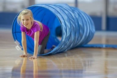 Ein blondes Mädchen im Grundschulalter spielt am AOK-Sportel-Sonntag in einem blauen Kriechtunnel.