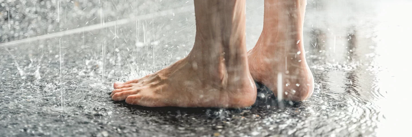 Jemand steht in einer Dusche, wo Fußpilz leicht übertragen werden kann.