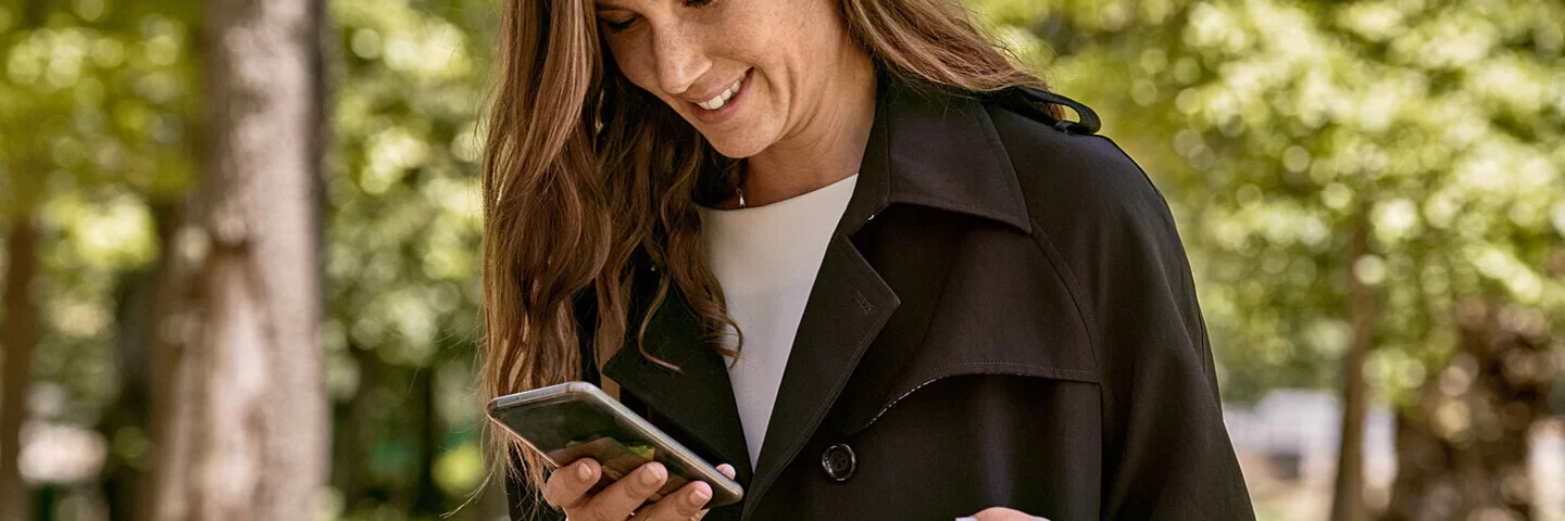 Eine Frau ist draußen unterwegs und liest Texte auf ihrem Smartphone. Sie weiß, dass die AOK Datenschutz-Richtlinien umsetzt.