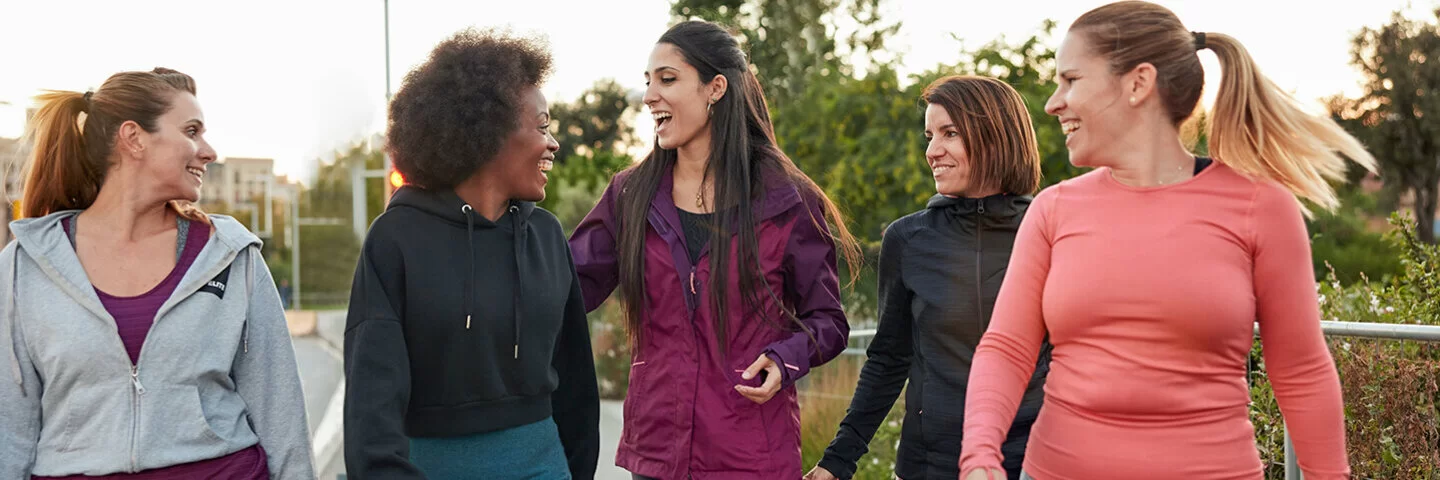 	  Fünf Frauen sind in Sportkleidung gekleidet. Sie gehen zu einem Sportplatz und unterhalten sich dabei.