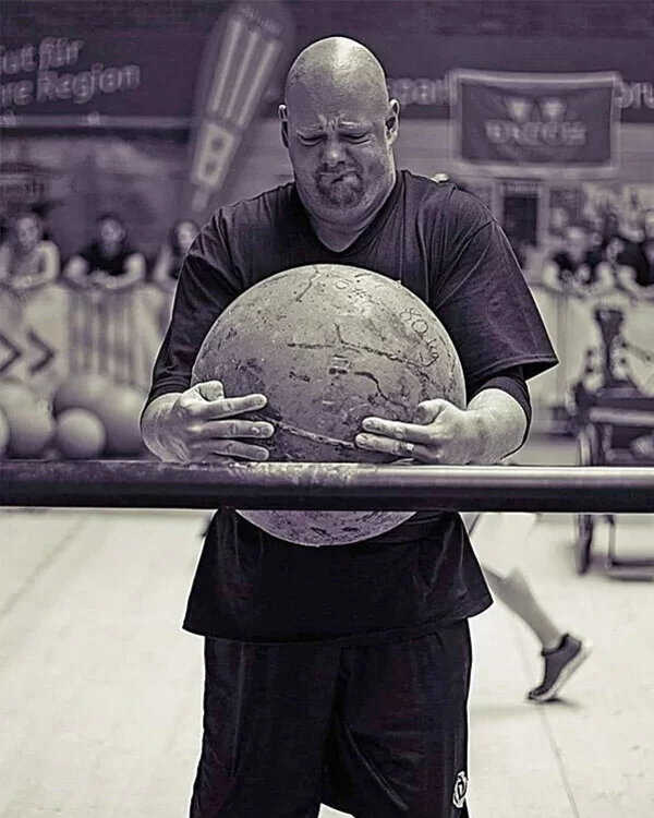Heinz Gräwe hebt bei einem Strongman Wettbewerb einen schweren Stein an.