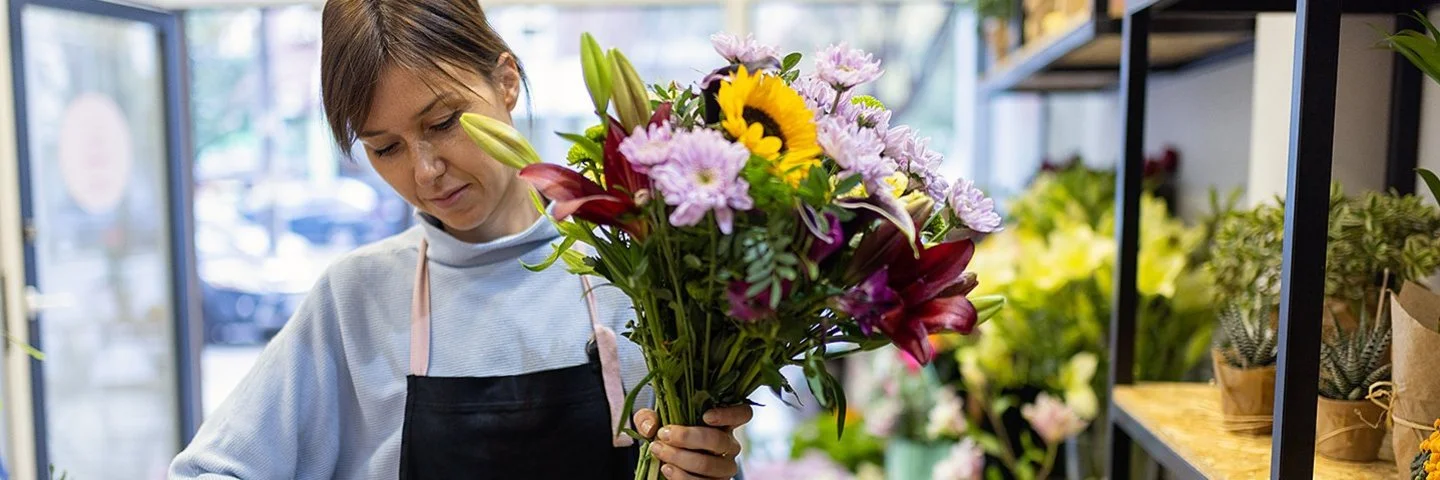 Eine Blumenfachverkäuferin stutzt im Geschäft einen Strauß.