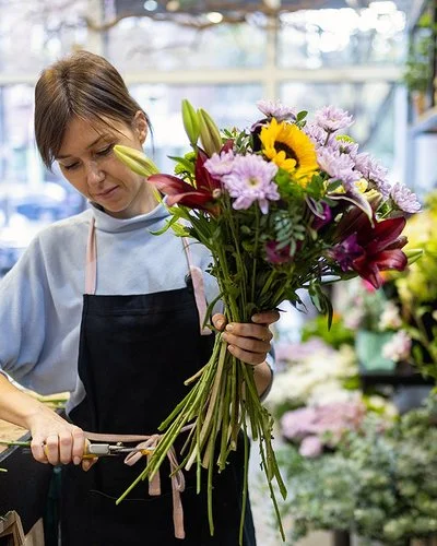 Eine Blumenfachverkäuferin stutzt im Geschäft einen Strauß.