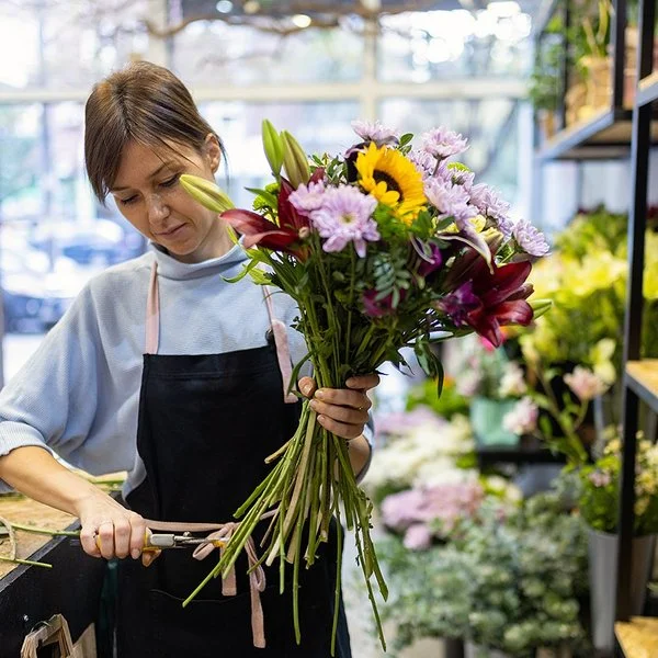 Eine Blumenfachverkäuferin stutzt im Geschäft einen Strauß.