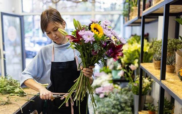 Eine Blumenfachverkäuferin stutzt im Geschäft einen Strauß.