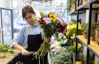 Eine Blumenfachverkäuferin stutzt im Geschäft einen Strauß.