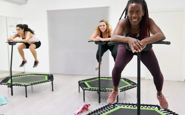 Eine Gruppe Frauen in Sportkleidung trainiert in einem Sportraum auf Mini-Trampolinen.