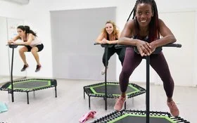 Eine Gruppe Frauen in Sportkleidung trainiert in einem Sportraum auf Mini-Trampolinen.