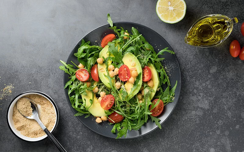 Rucculasalat mit Avocado und Tomaten, der mit Hefeflocken verfeinert wurde.