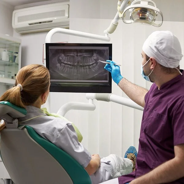 Ein Zahnarzt erklärt seiner Patientin eine Wurzelbehandlung anhand eines Röntgenbilds.
