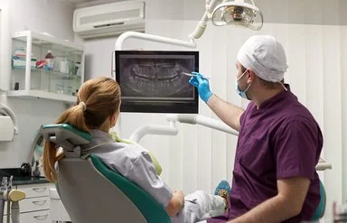 Ein Zahnarzt erklärt seiner Patientin eine Wurzelbehandlung anhand eines Röntgenbilds.