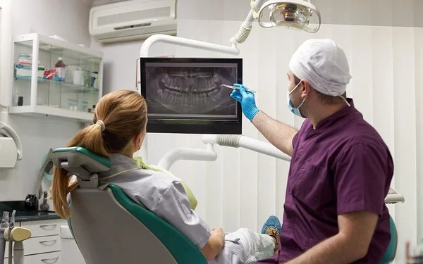 Ein Zahnarzt erklärt seiner Patientin eine Wurzelbehandlung anhand eines Röntgenbilds.