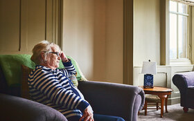 Eine ältere Frau sitzt auf der Couch und starrt in die Leere, sie ist einsam.