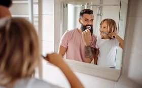 Ein Mann und ein kleines Mädchen schauen in einen Badezimmerspiegel, während sie sich die Zähne putzen.