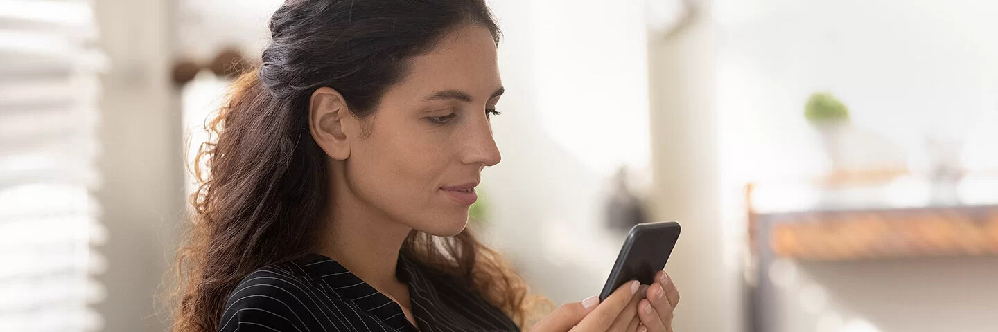 Eine junge Frau mit langen dunklen Haaren schaut nachdenklich auf ihr Smartphone.