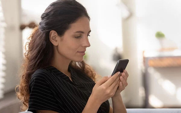 Eine junge Frau mit langen dunklen Haaren schaut nachdenklich auf ihr Smartphone.