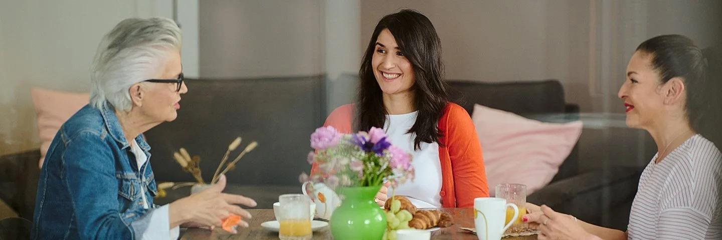 Drei Frauen unterschiedlichen Alters sitzen an einem Tisch mit Frühstück und sprechen über das Älterwerden.