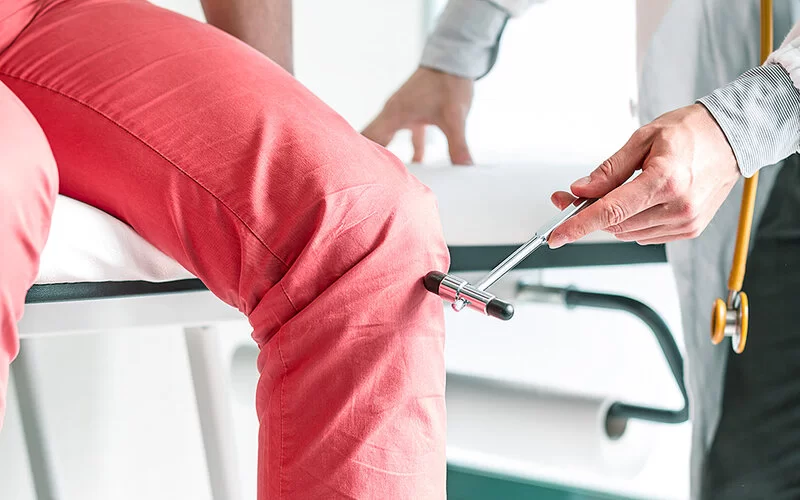 Ein Neurologe klopft mit einem Reflexhammer auf das Knie eines Patienten.