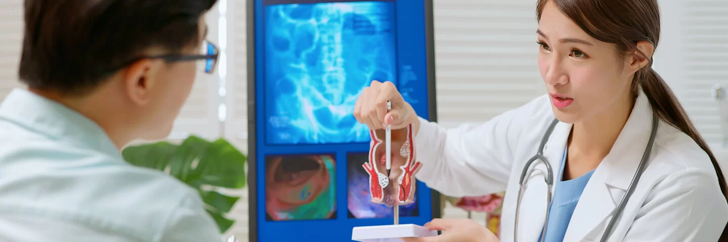 Eine Ärztin erklärt einem Patienten anhand eines anatomischen Modells, wo Darmpolypen liegen können.