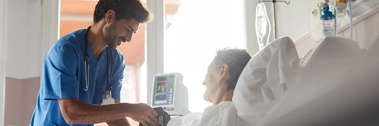 Ein Krankenpfleger misst den Puls einer im Krankenhausbett liegenden Patientin.
