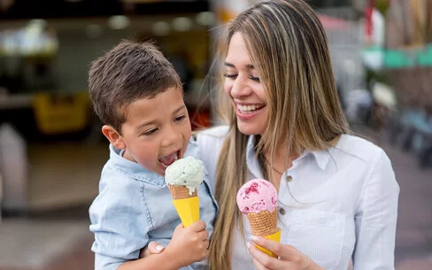 Eis aus der Eisdiele: Eine Mutter hat ihren Sohn auf dem Arm, beide essen eine Kugel in der Waffel.