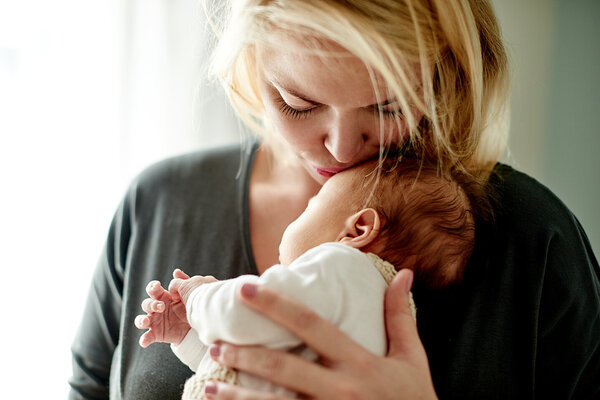 Eine junge Mutter hält ihr Baby im Arm und küsst es auf die Stirn.