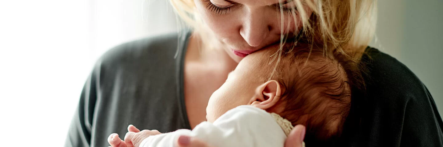 Eine junge Mutter hält ihr Baby im Arm und küsst es auf die Stirn.