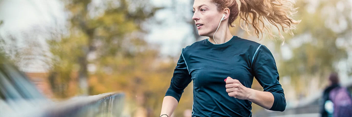 Eine junge Frau joggt über eine Brücke und hört dabei Musik.