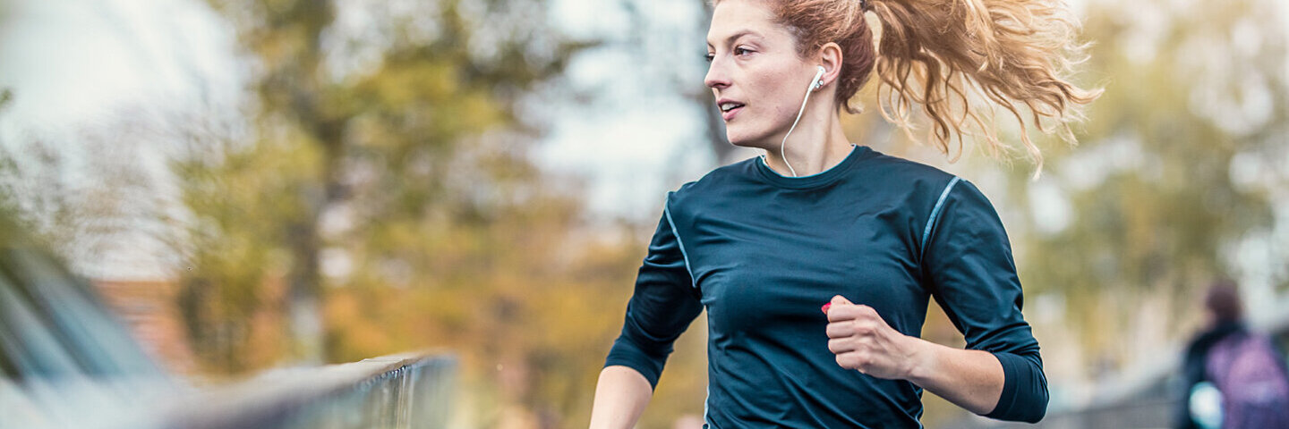 Eine junge Frau joggt über eine Brücke und hört dabei Musik.